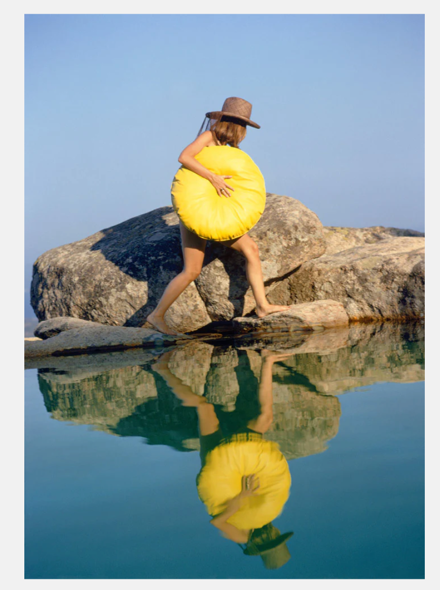 Person holding a yellow object near a body of water with a clear blue sky.