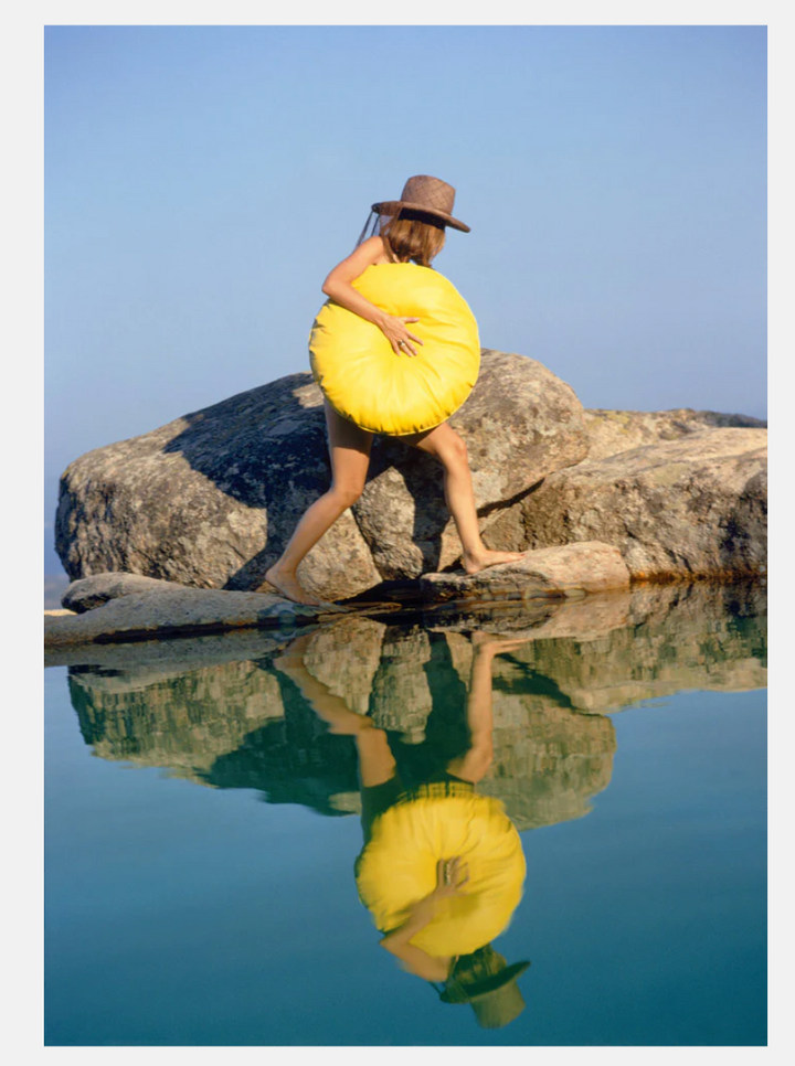 Person holding a yellow object near a body of water with a clear blue sky.