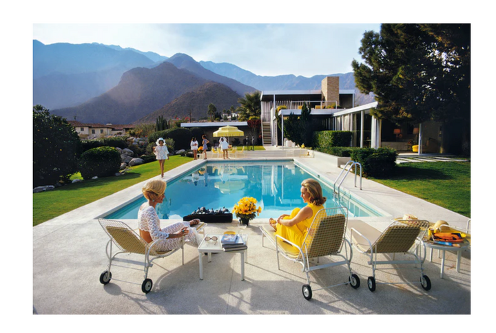 Two women sitting by a pool with mountains in the background