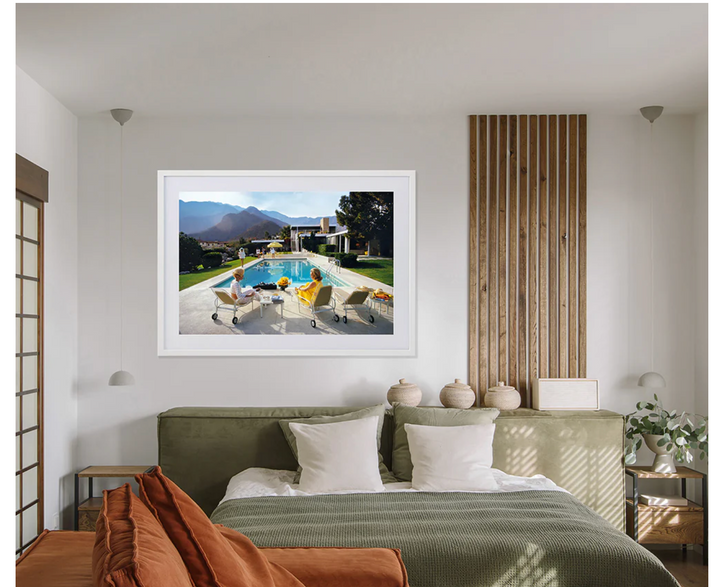 Room interior with a framed picture of a pool scene on the wall above a bed.