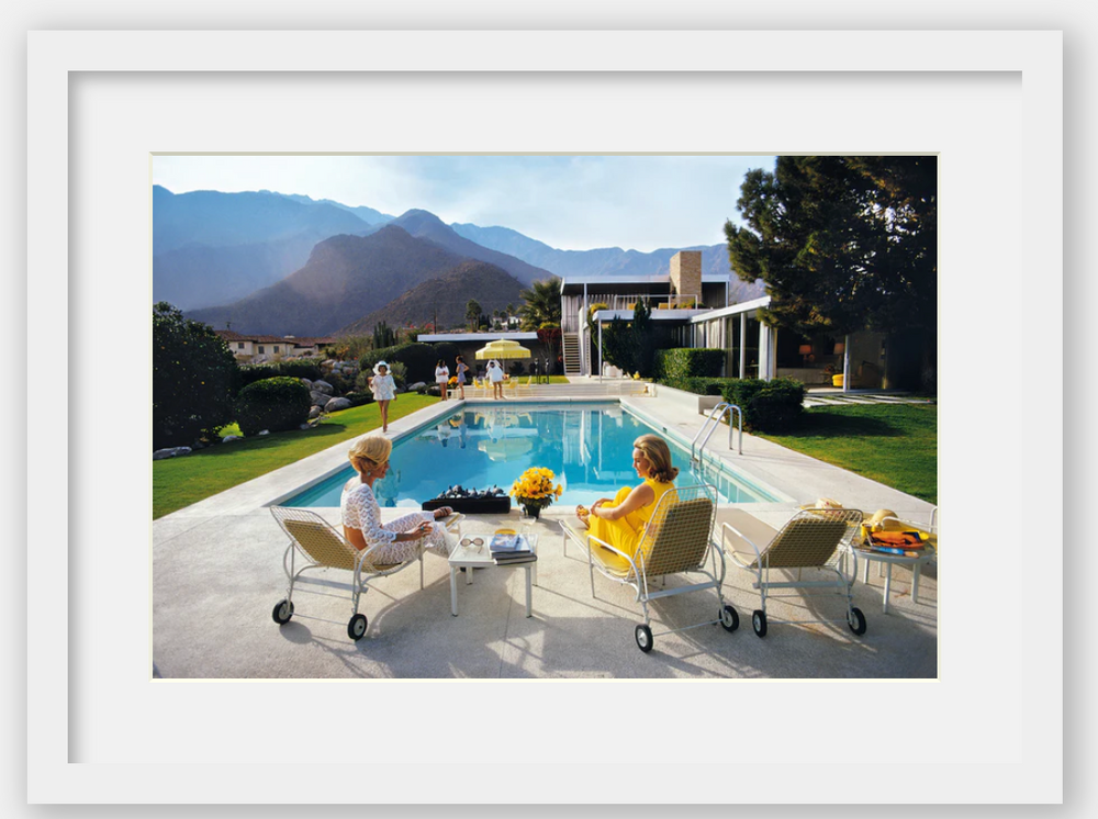 Two women sitting by a pool with mountains in the background