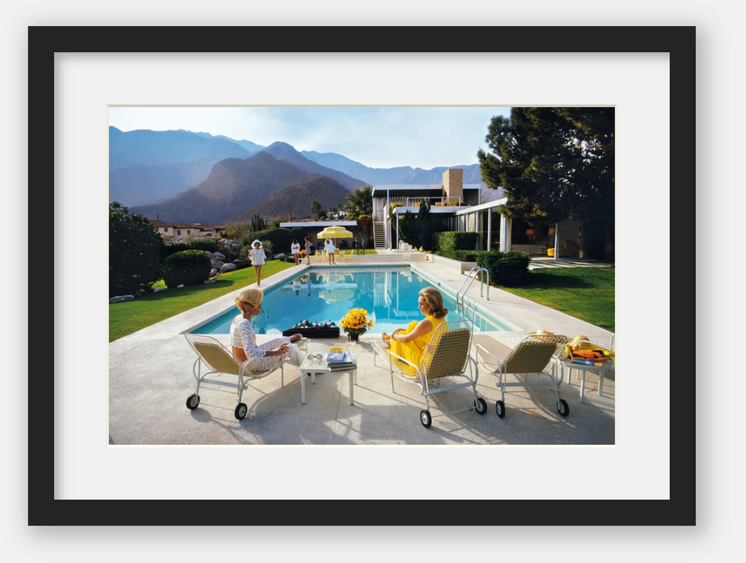 Two women sitting by a pool with mountains in the background